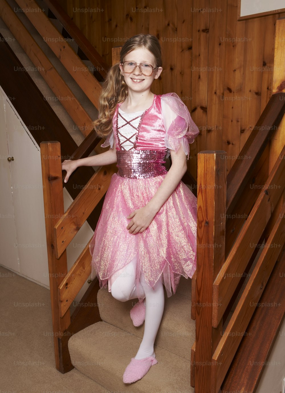 a little girl in a pink dress standing on some stairs