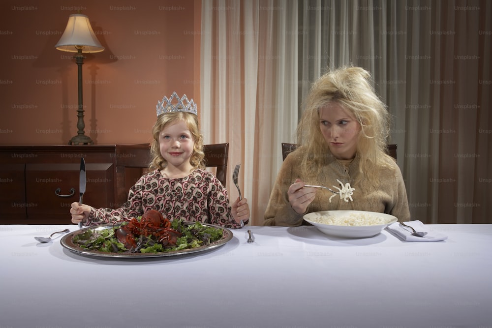 Girl wearing crown and eating lobster, woman with tousled hair eating pasta