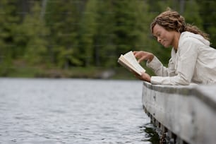a woman sitting on a dock reading a book