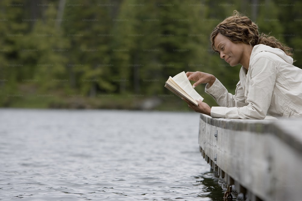 a woman sitting on a dock reading a book