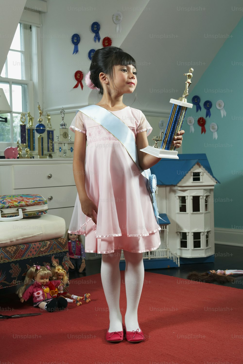 a little girl in a pink dress holding a trophy