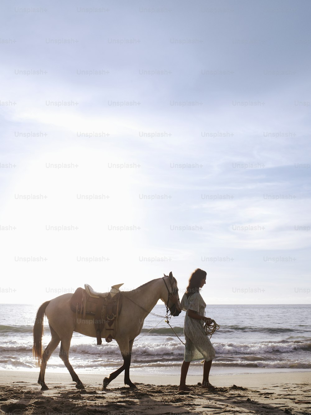 a woman is walking a horse on the beach