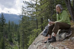 Une femme assise au sommet d’un rocher à côté d’une forêt