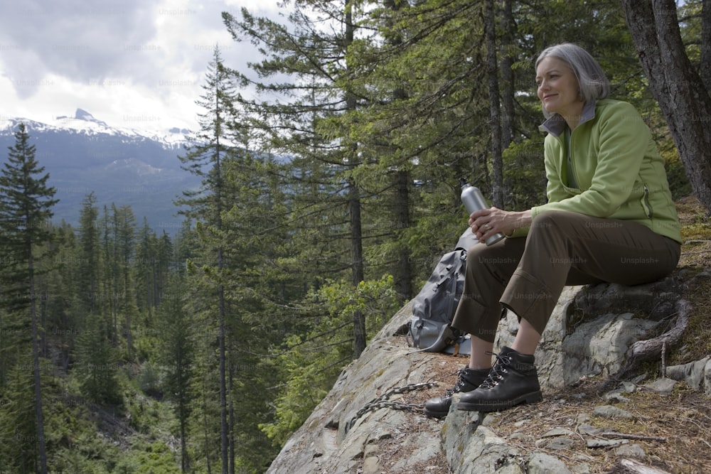Una mujer sentada en la cima de una roca junto a un bosque