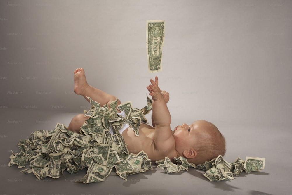 a baby laying on its back on a pile of money