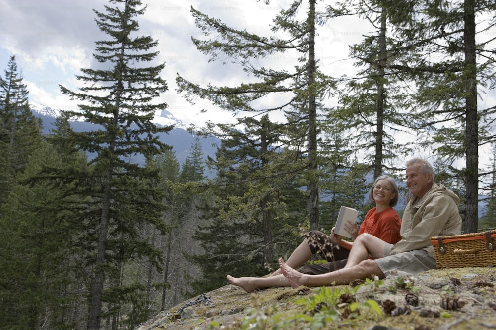 a man and a woman sitting on a rock in the woods