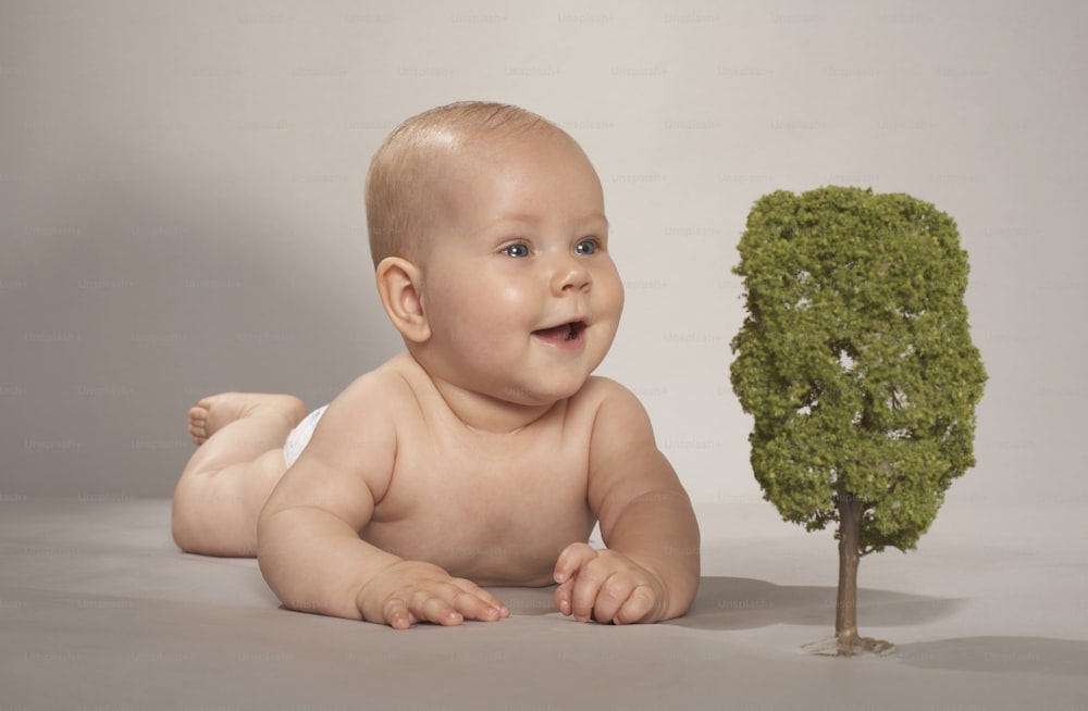 a baby sitting next to a small tree