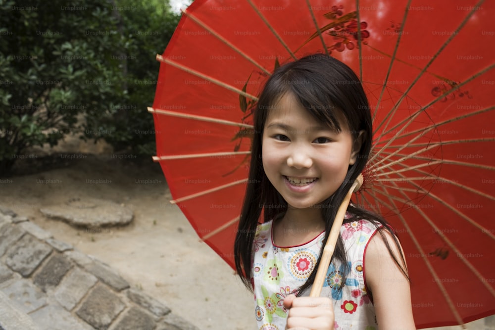 Una niña pequeña sosteniendo un paraguas rojo y sonriendo