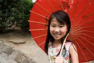 Una niña pequeña sosteniendo un paraguas rojo y sonriendo
