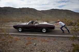 a man pushing a convertible car down the road