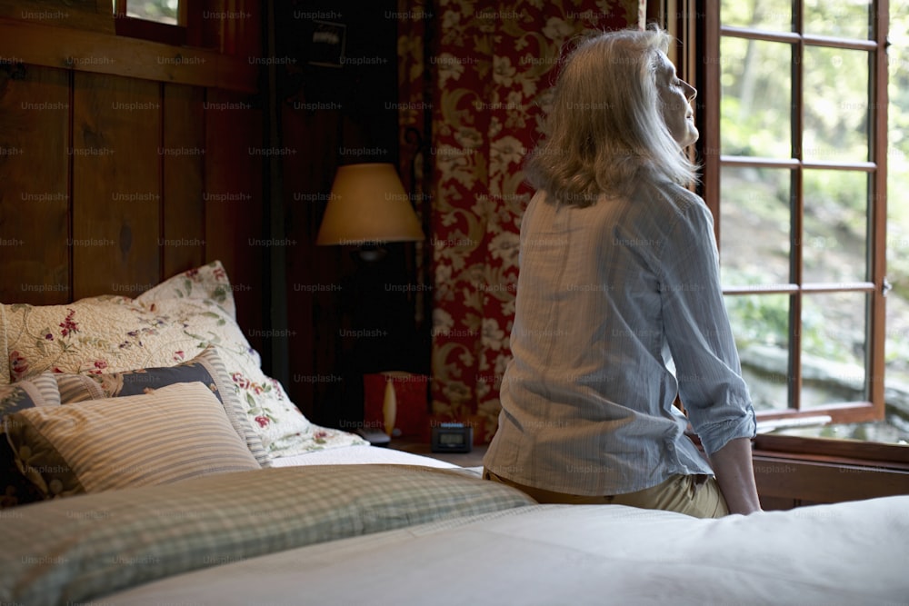 uma mulher em pé em uma cama olhando pela janela