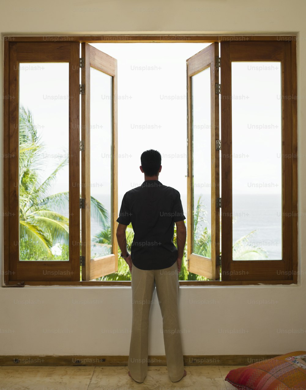 a man standing in front of a window looking out at the ocean
