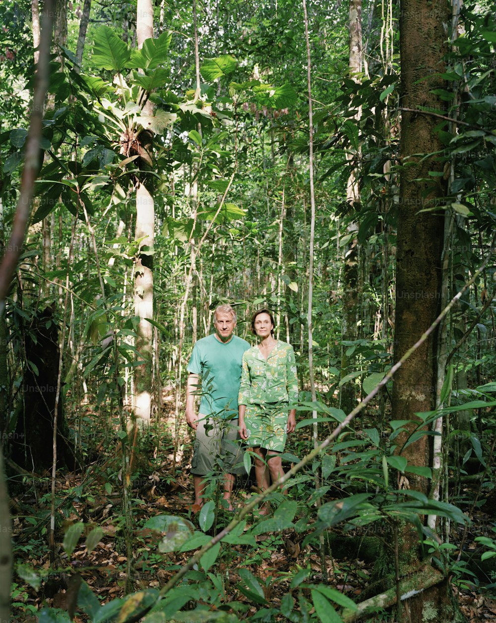 a man and woman standing in the middle of a forest
