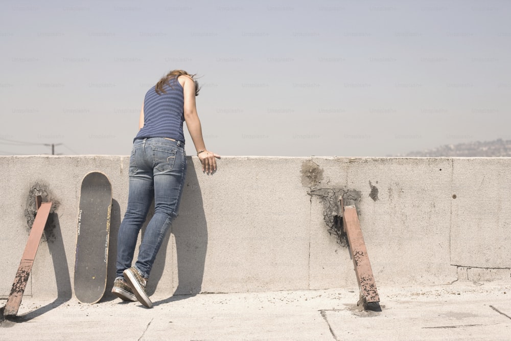 a woman leaning against a wall with a skateboard