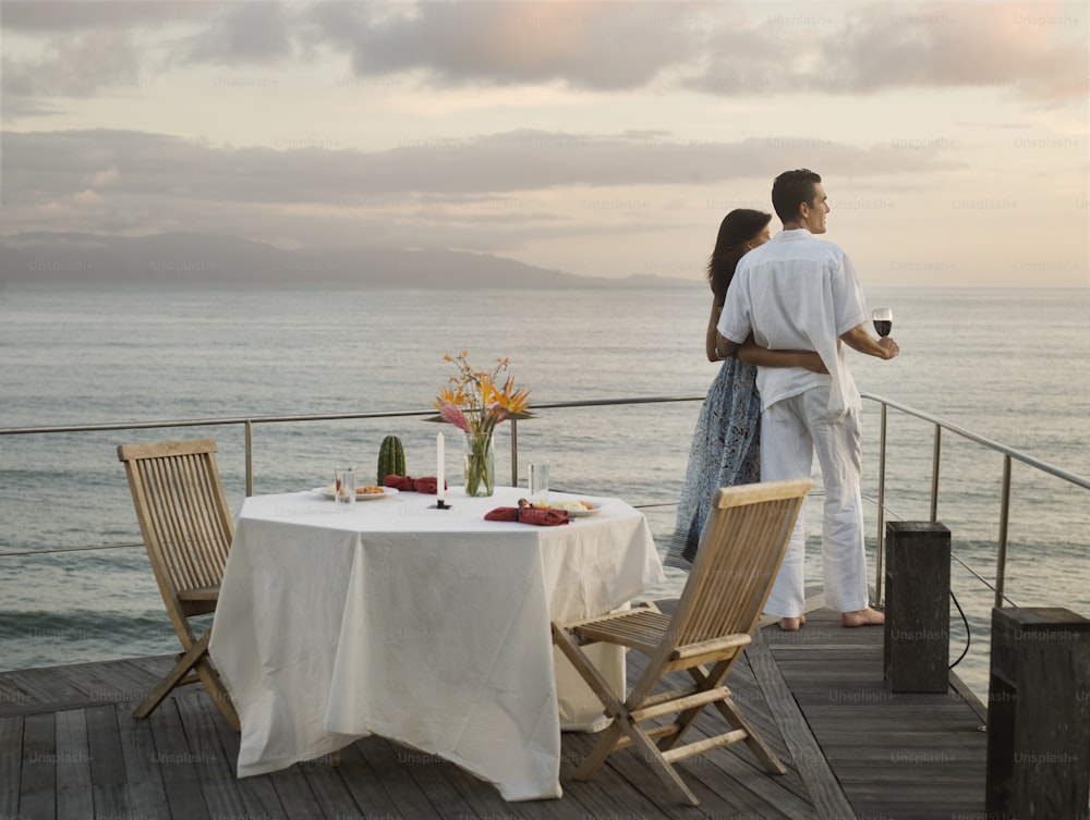 a man and a woman are standing on a deck overlooking the ocean