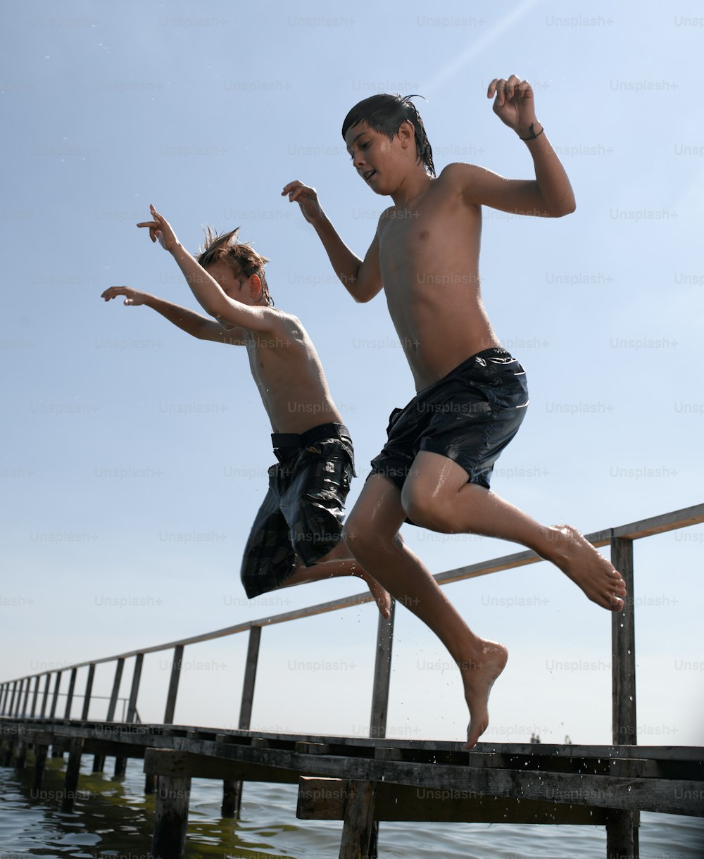 Dos niños saltando de un muelle al agua