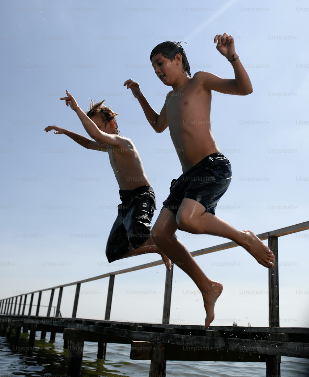 two boys jumping off a dock into the water