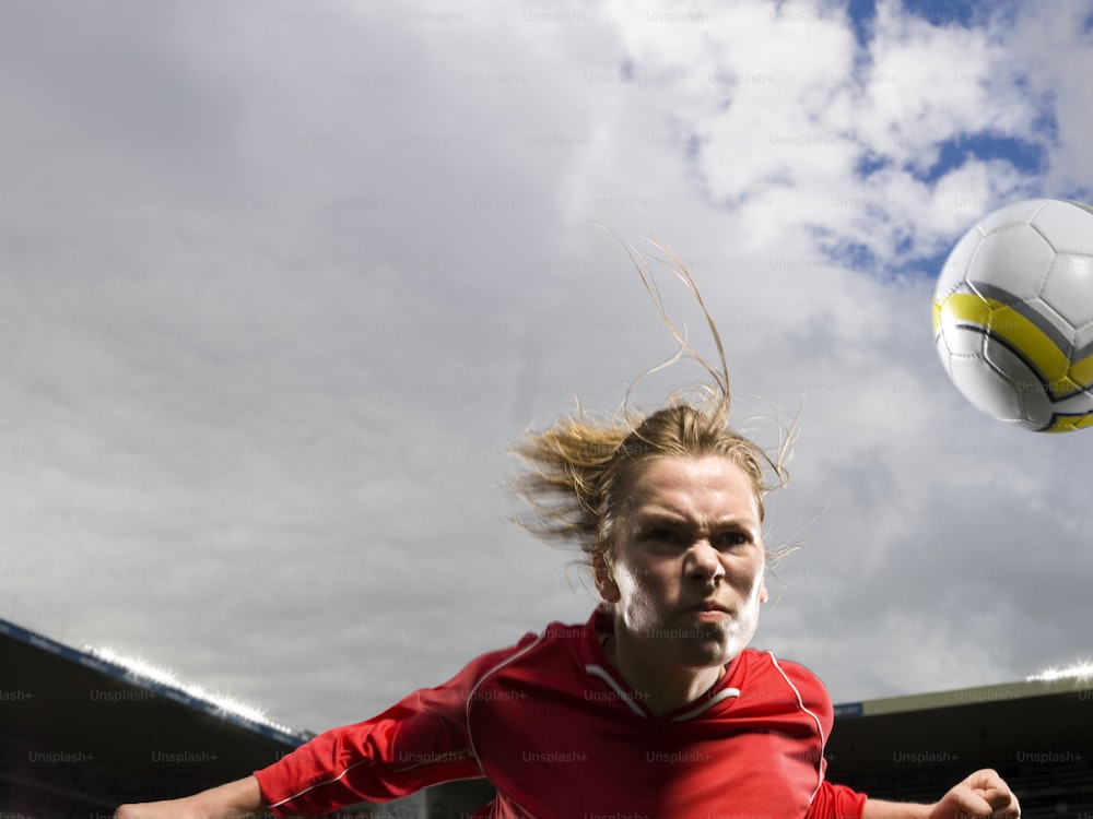 a woman in a red shirt is playing with a soccer ball