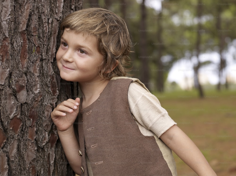 a little boy standing next to a tree