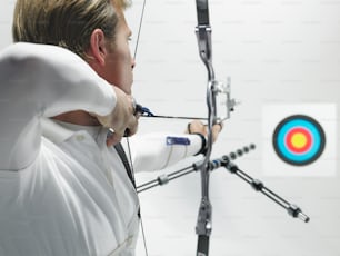 a man in a white shirt is aiming a bow at a target