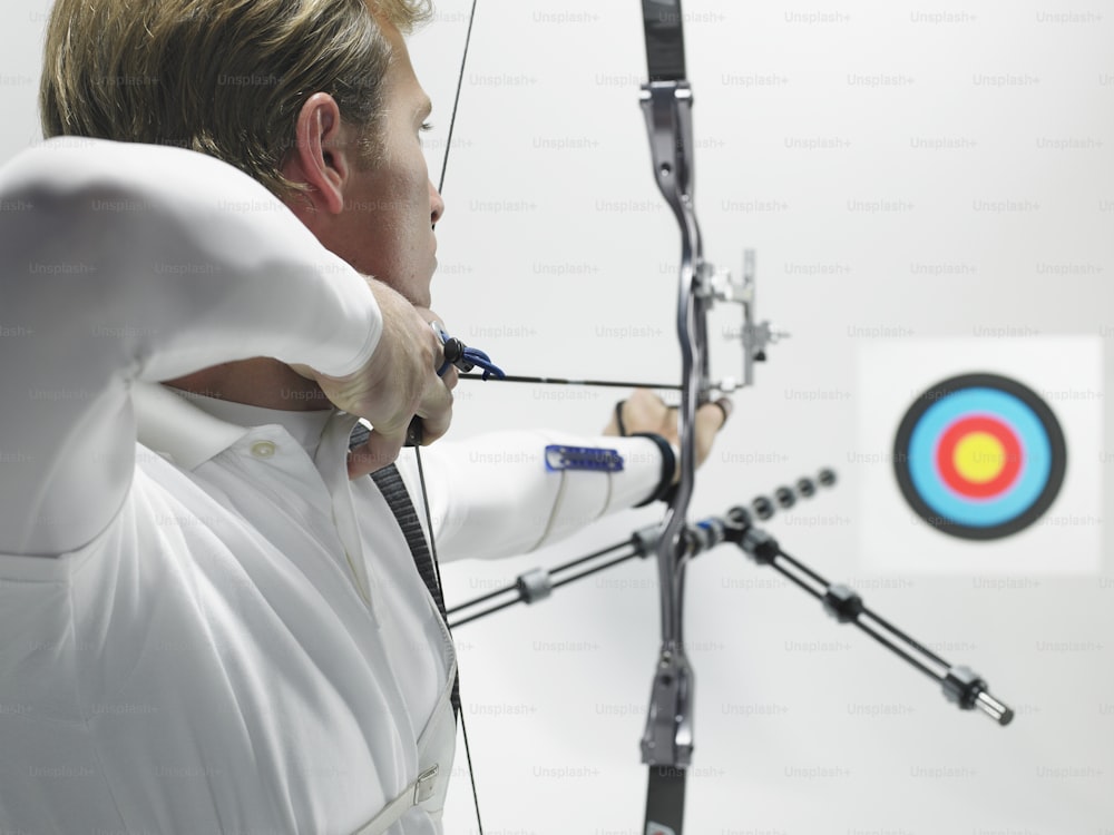 a man in a white shirt is aiming a bow at a target