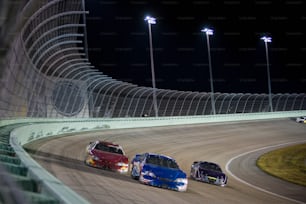 three cars racing on a track at night