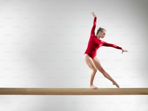 a woman in a red leotard balances on a beam
