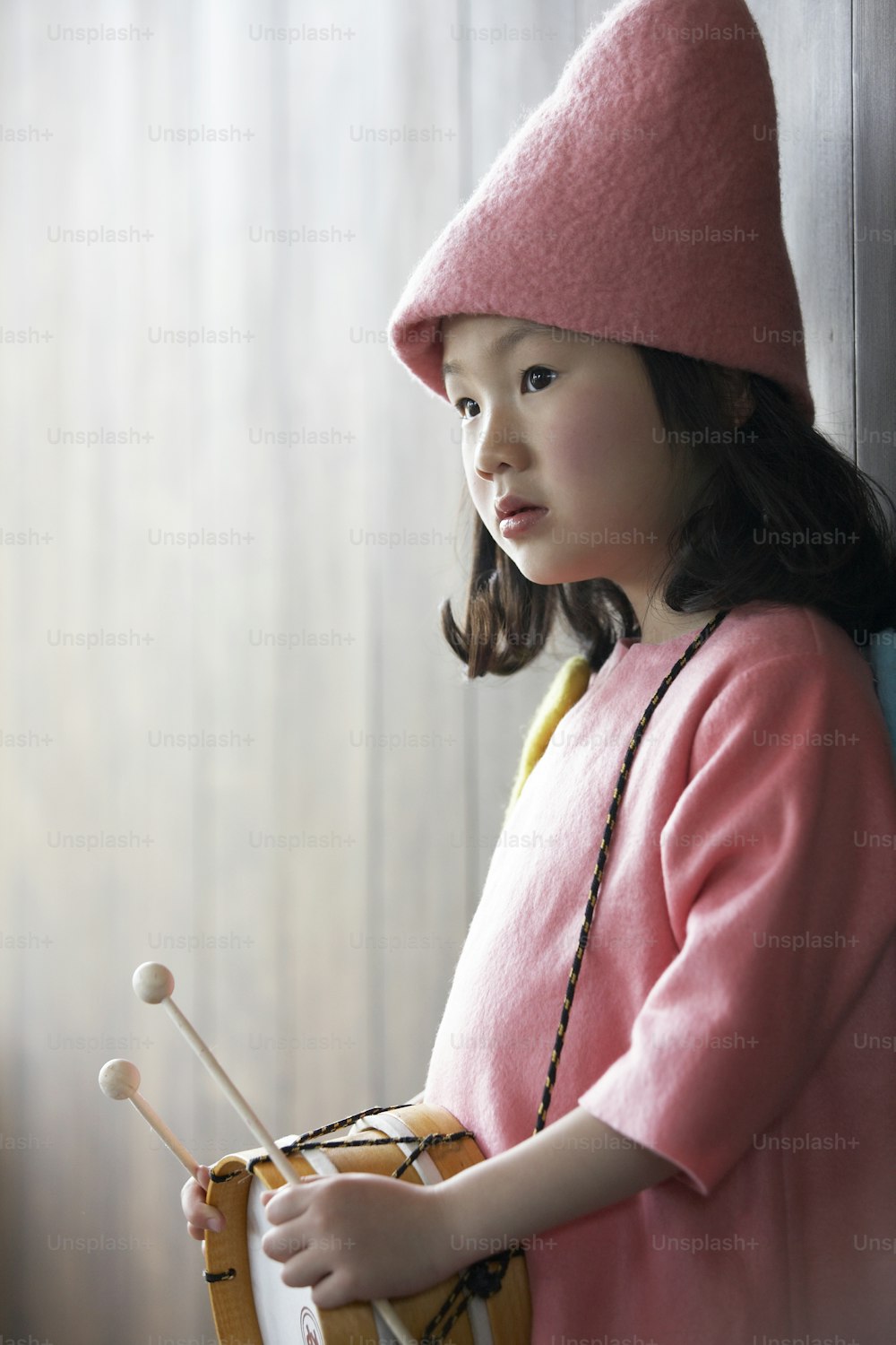 Ein kleines Mädchen, das einen rosa Hut trägt und eine Trommel hält