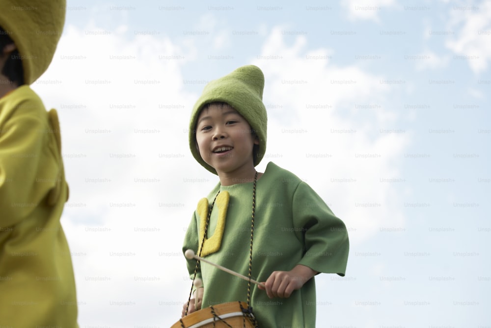 a young boy in a green outfit holding a drum