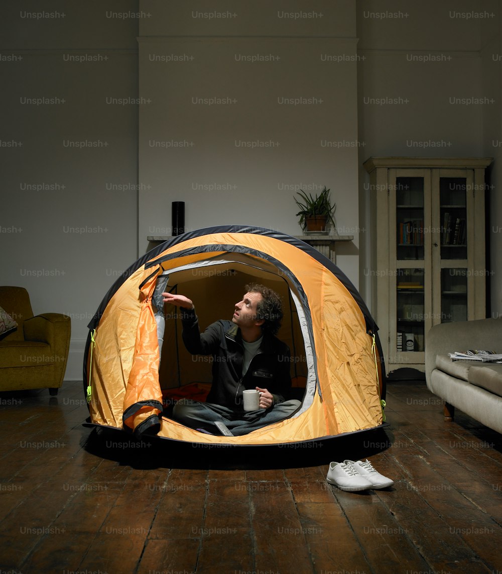 a man sitting inside of a tent on top of a wooden floor