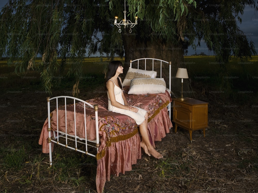 a woman sitting on a bed under a tree