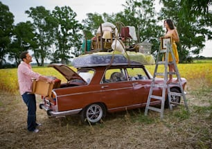 a man and a woman standing next to a car with luggage on top of it