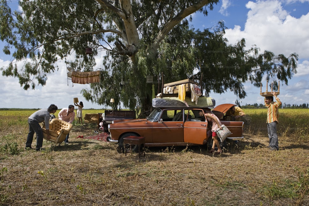 um grupo de pessoas em pé ao redor de um carro em um campo