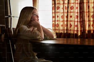a girl sitting at a table with her hand on her chin