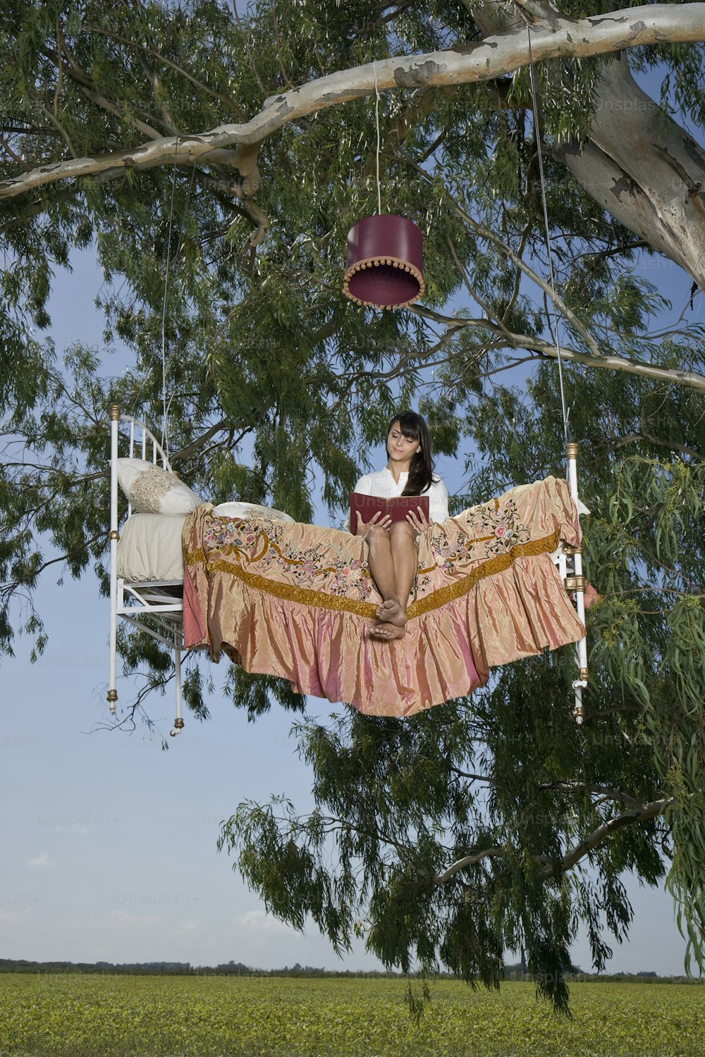 a woman sitting on a bed suspended from a tree