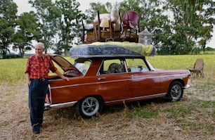 um homem parado ao lado de um carro velho com bagagem em cima dele