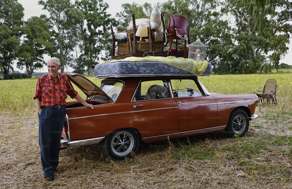 a man standing next to an old car with luggage on top of it