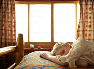 Una niña acostada encima de una cama junto a una ventana