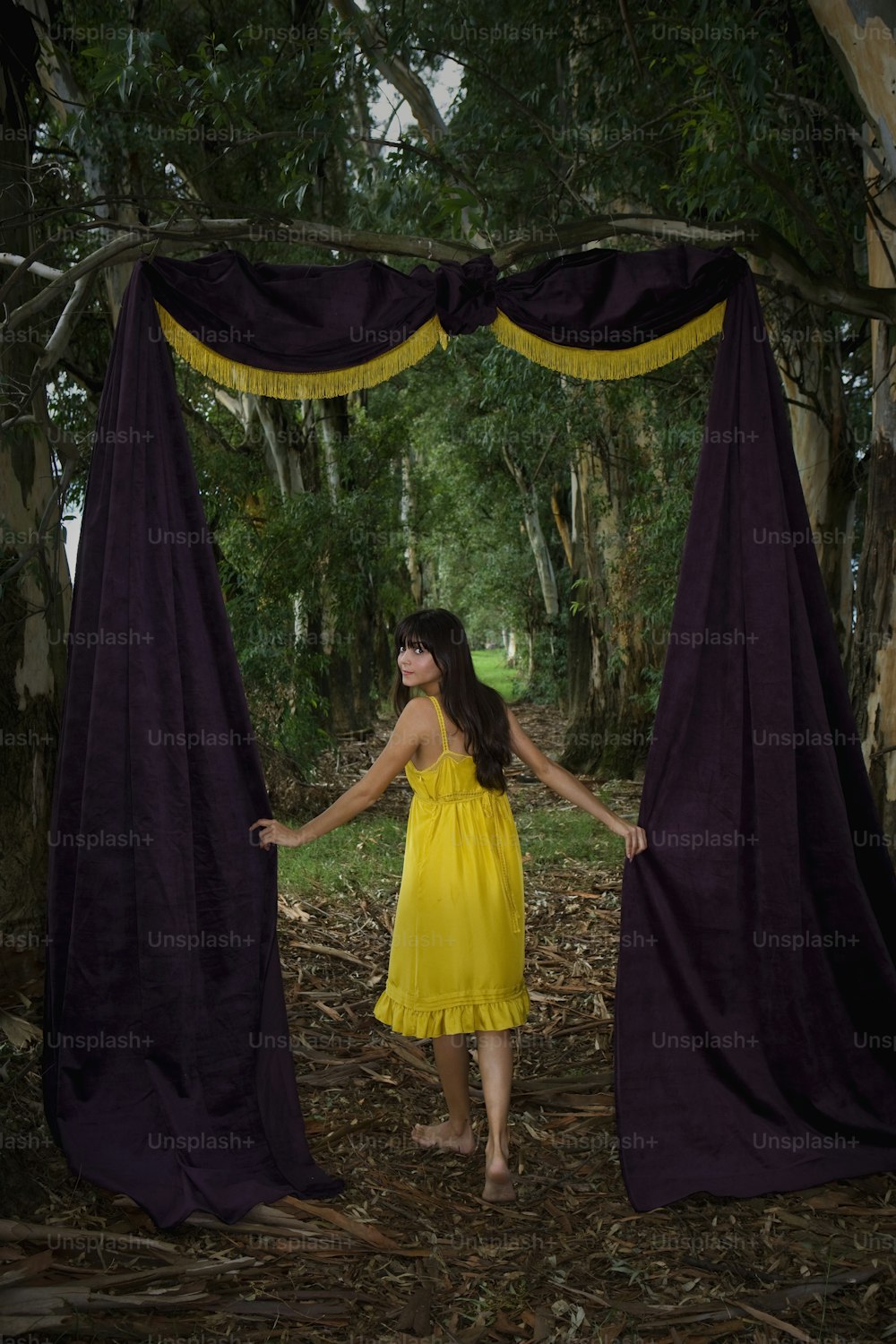 a woman in a yellow dress standing in front of a purple curtain