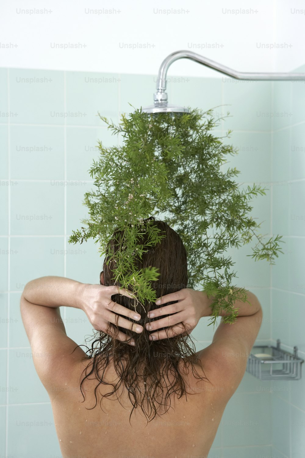 욕조에 있는 여자가 머리 위로 식물을 들고 있다