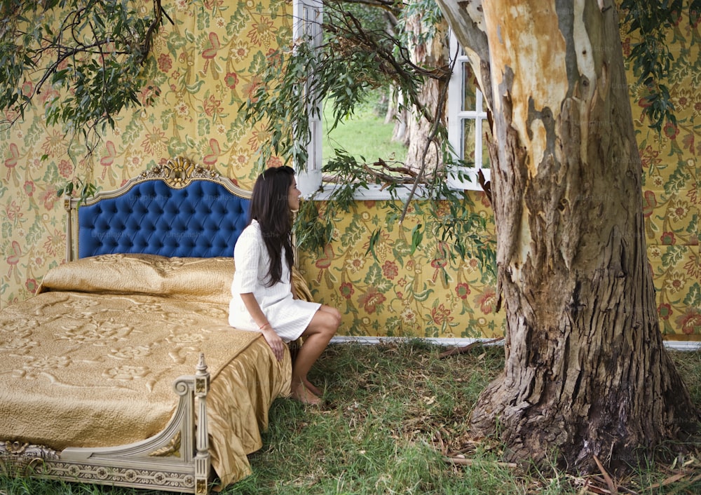 a woman sitting on a bed next to a tree