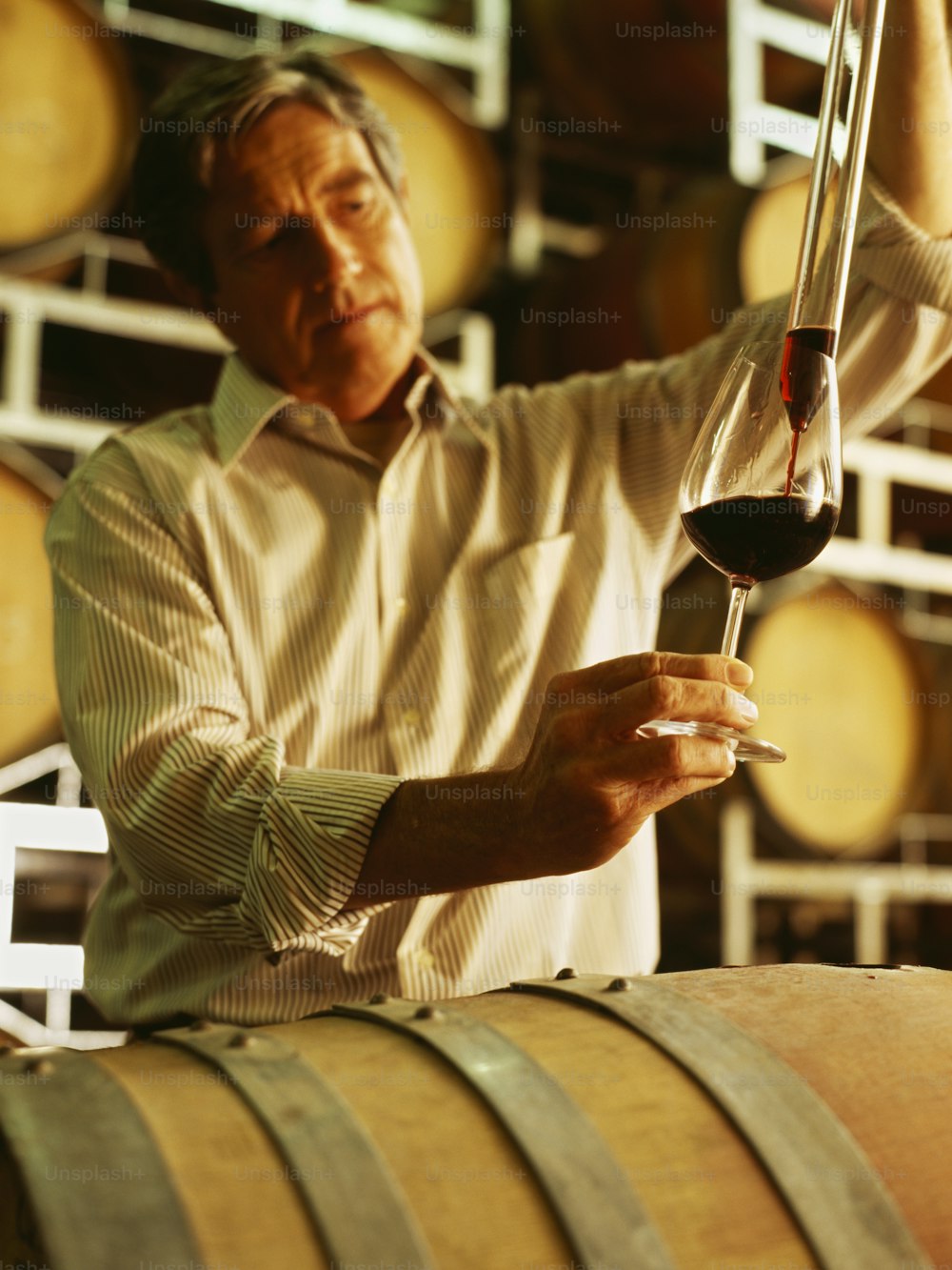 a man holding a glass of wine in front of barrels