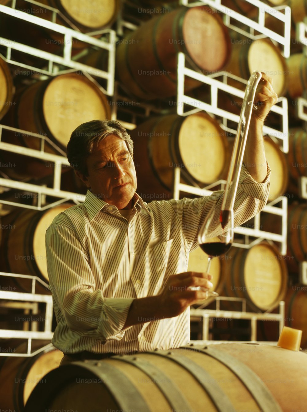 a man holding a glass of wine in front of barrels