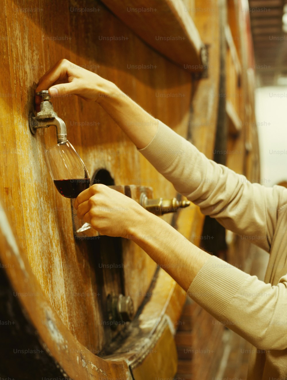 a woman pouring a glass of wine into a wooden barrel