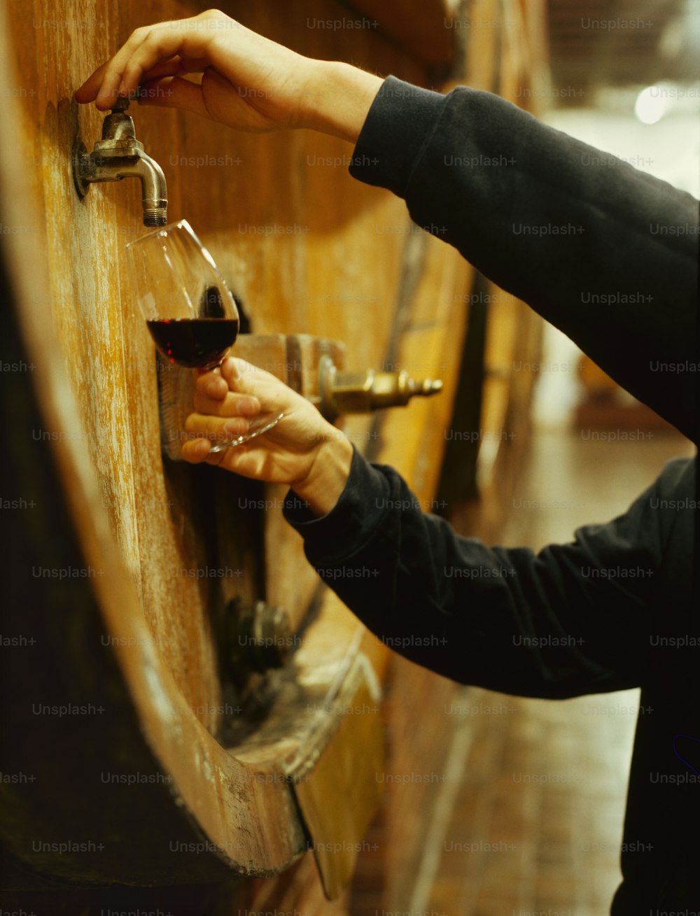 a person holding a glass of wine in front of a wooden barrel