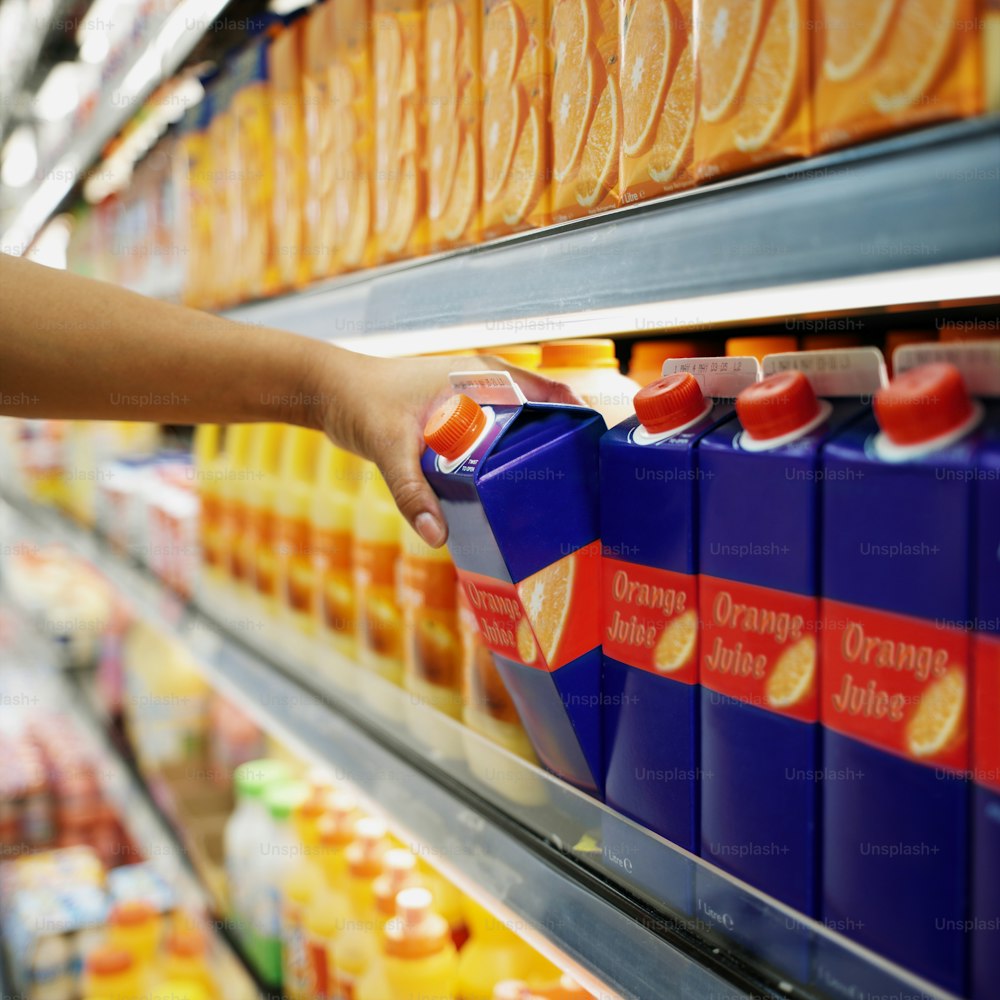 a hand reaching for a carton of orange juice