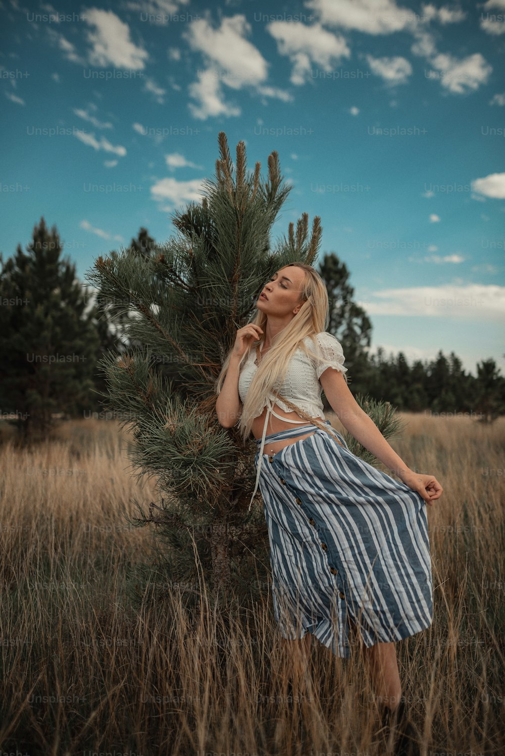 uma mulher em pé em um campo ao lado de uma árvore