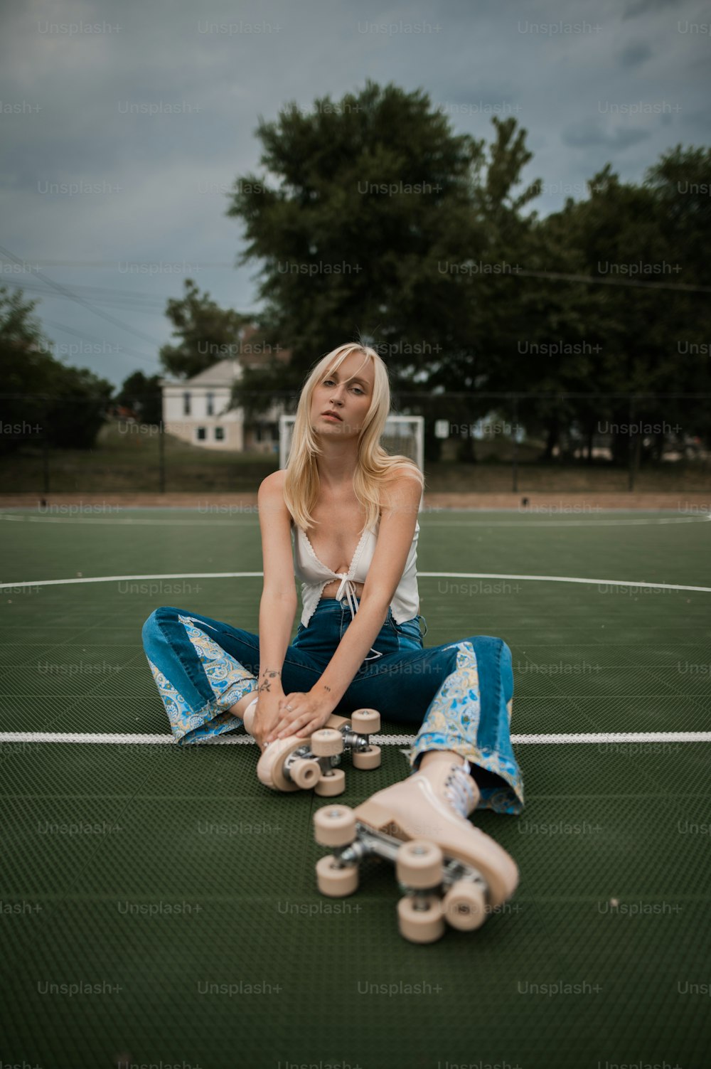 a woman sitting on a tennis court with her skateboard