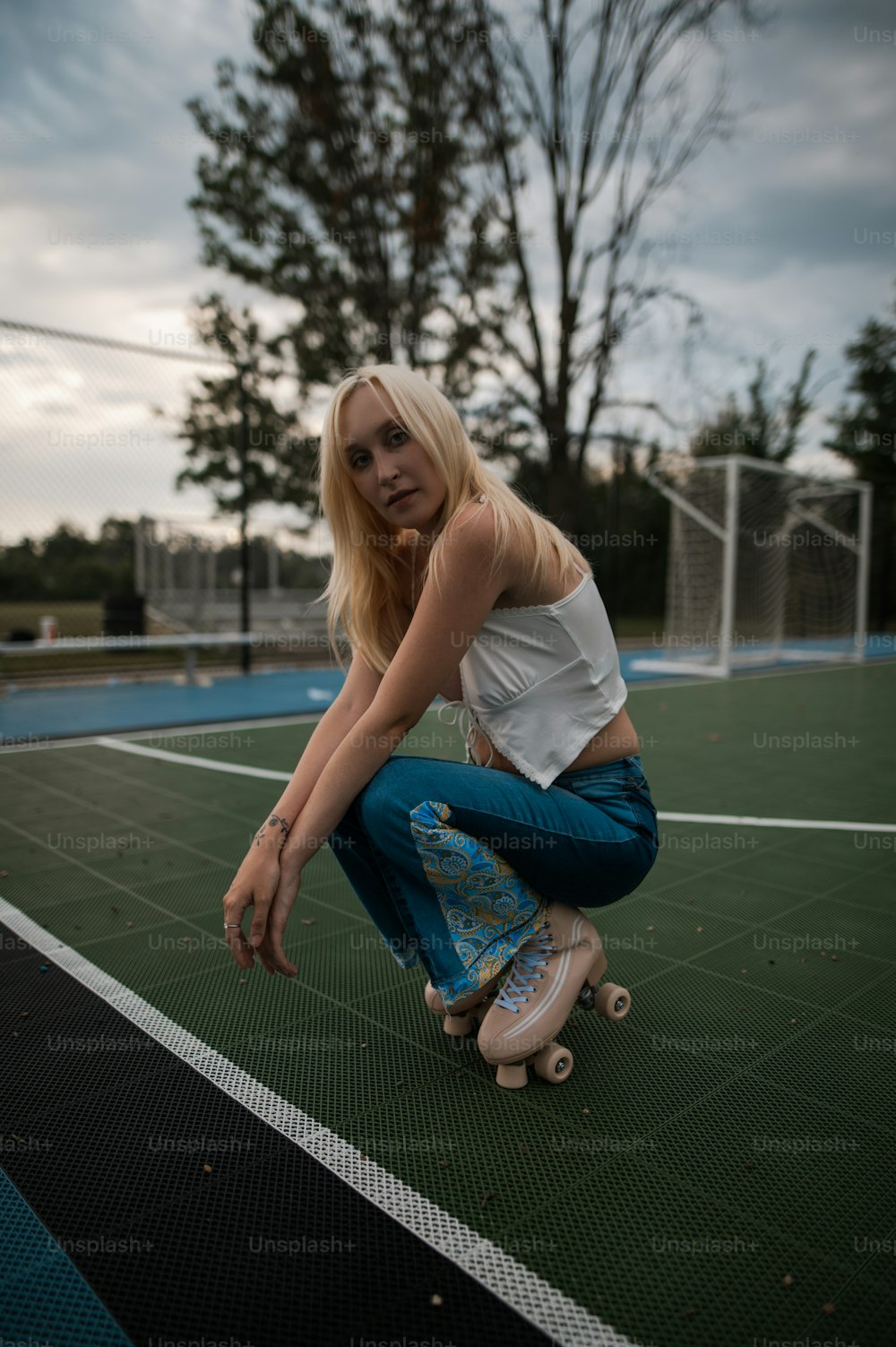 a woman kneeling on a tennis court holding a skateboard