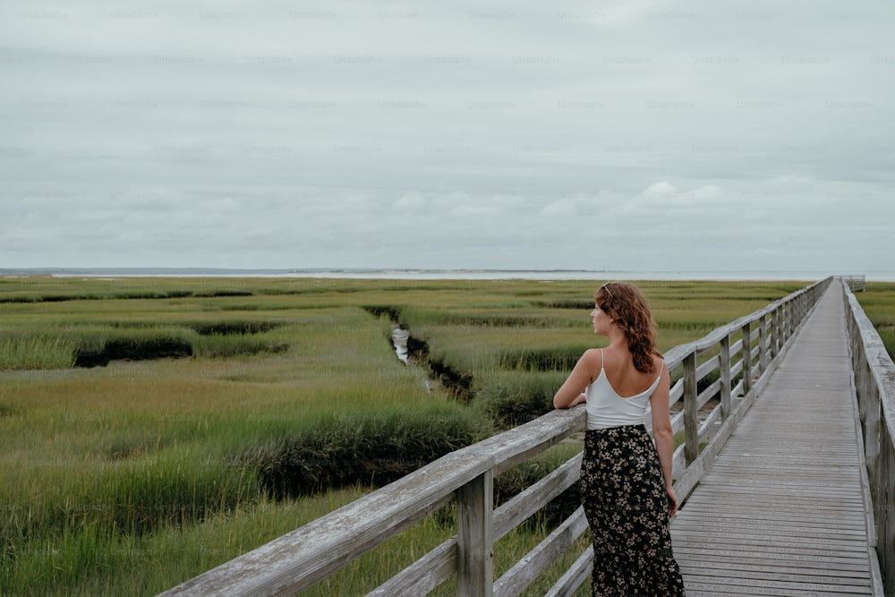 a woman standing on a boardwalk looking out over a marsh
